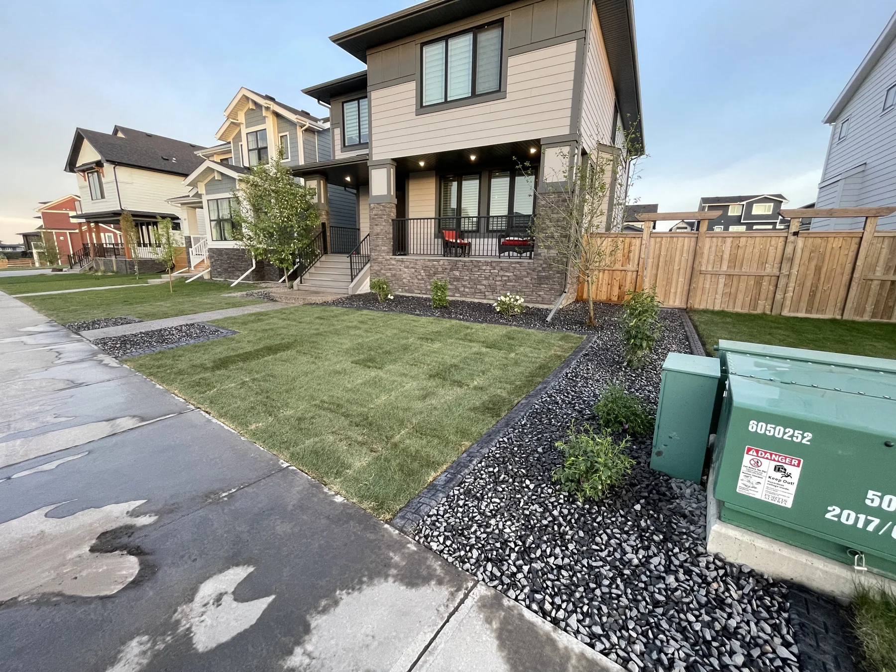 Completed front yard with fresh sod, young trees, shrubs, and decorative black rock