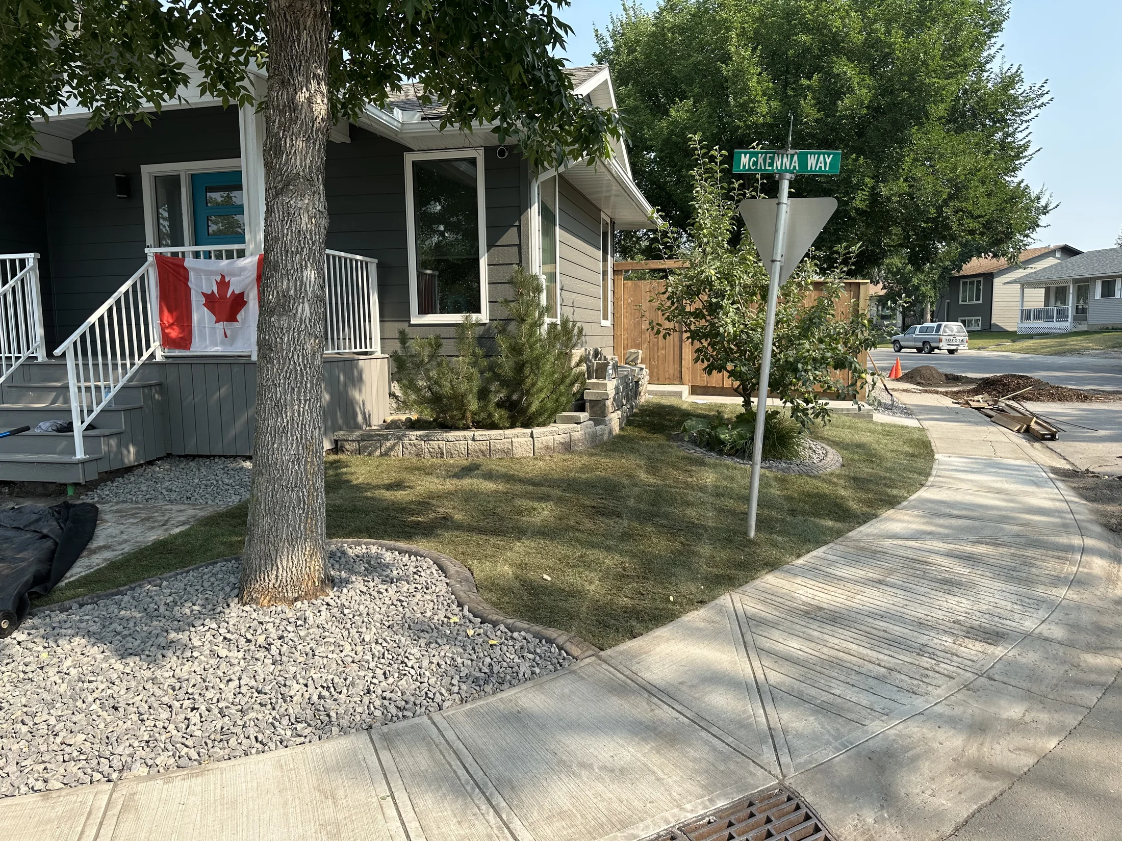 Corner-lot front yard with curved rock beds, a block retaining wall, mature trees, and a new privacy gate